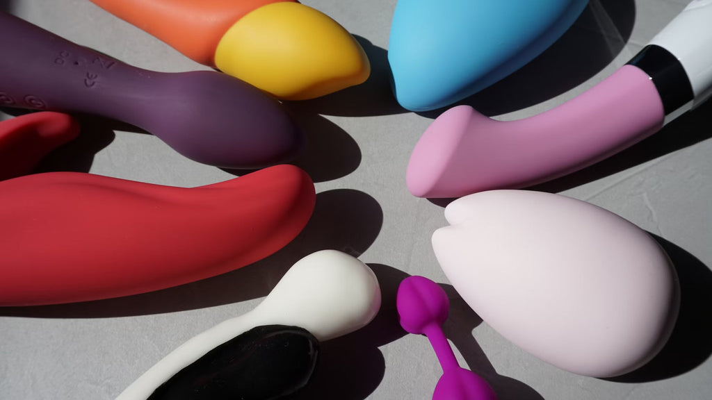 Close-up of a hand holding a blue silicone vibrator on a bed, representing modern vibrator types and pleasure products.